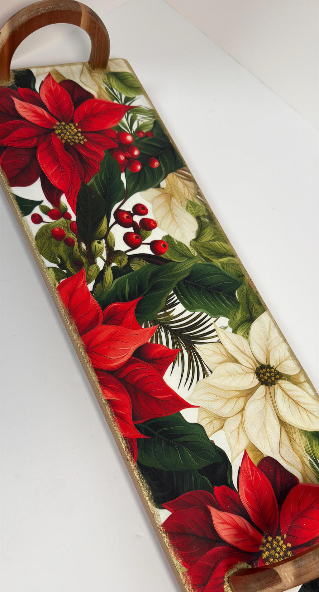 a wooden tray with a vibrant floral design, including red poinsettia flowers, green leaves, and red berries.