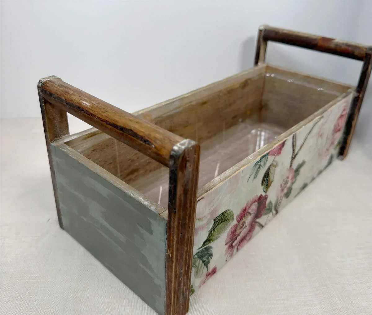 A wooden box with a floral pattern on the side, featuring a handle on the front.