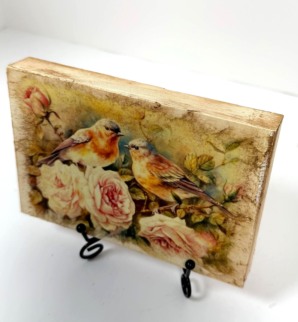 a wooden block with a painting of two birds perched on flowers, including roses.