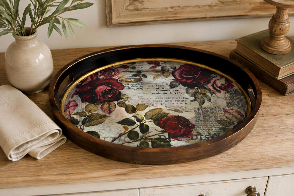 a wooden tray with a floral design on it, placed on a wooden surface. There is a vase with green leaves and a book nearby, creating a cozy and decorative atmosphere.