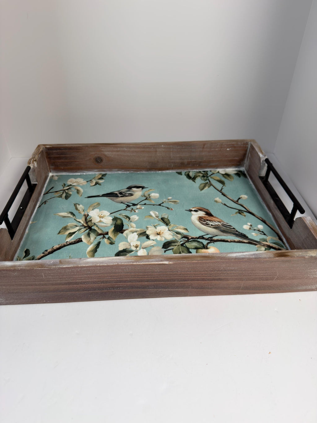 A wooden tray with a floral pattern on it, featuring two birds perched on branches.