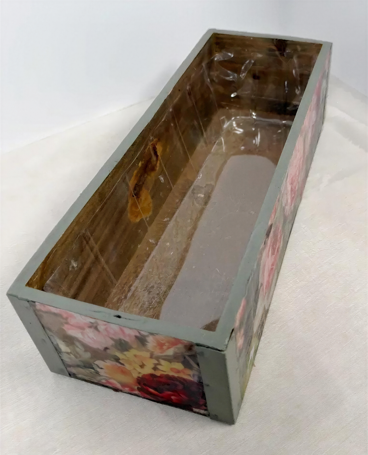 a wooden box with a floral pattern on its side, sitting on a white surface.