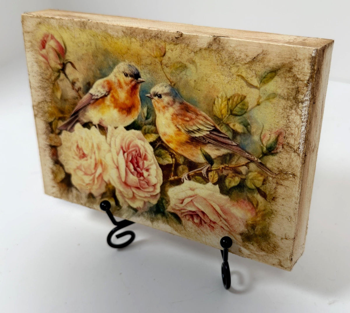 a wooden block with a painting of two birds perched on flowers, including roses.