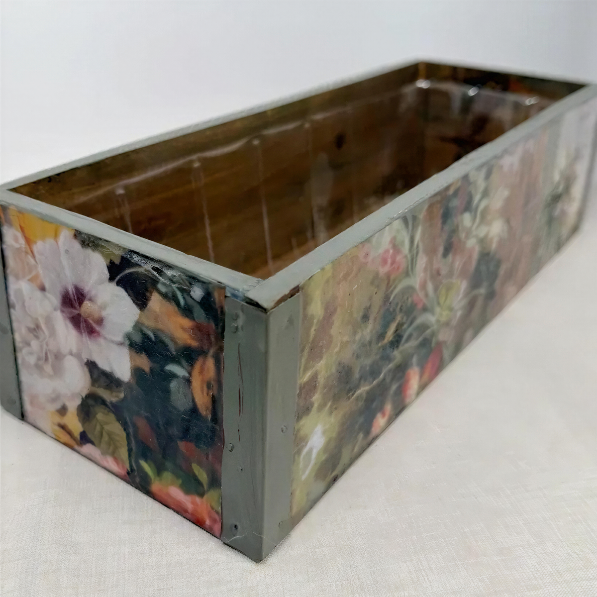 A wooden box with a floral pattern painted on it, sitting on a white surface.