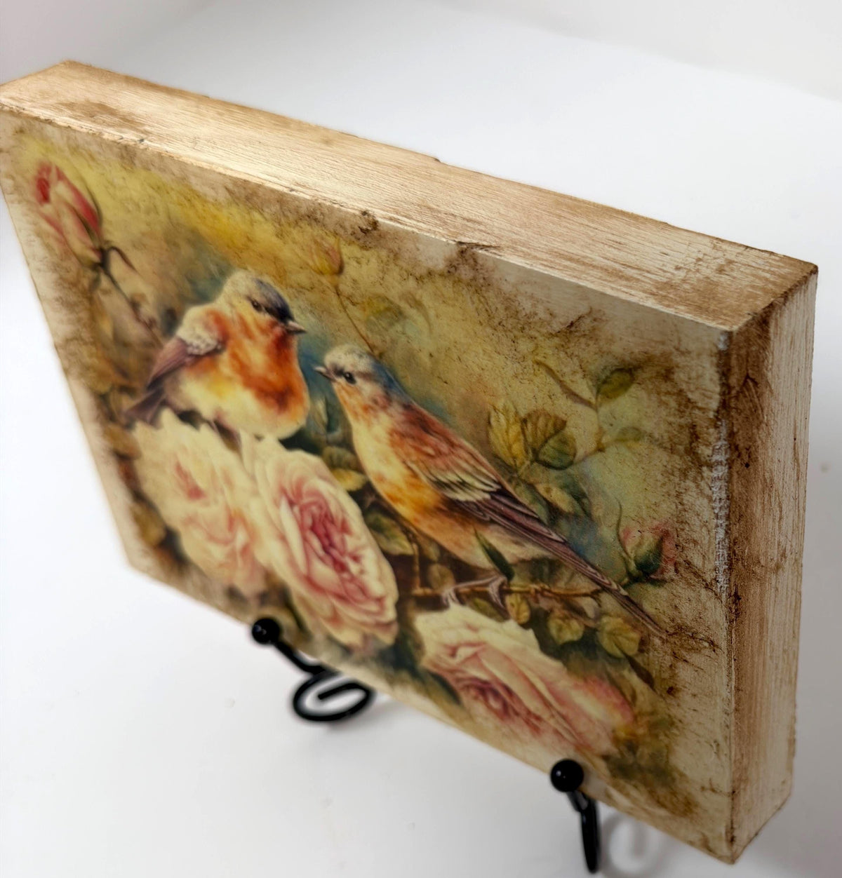 a wooden frame with a painting of two birds perched on branches with pink flowers.