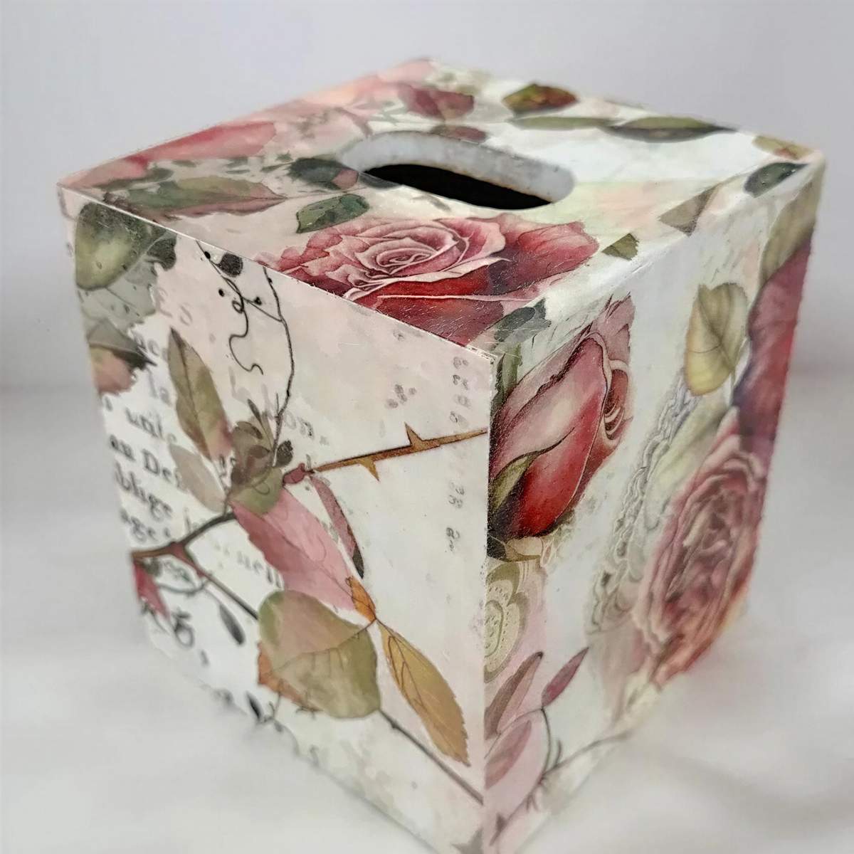 A decorative box with a floral pattern, featuring roses and leaves in shades of pink and green.