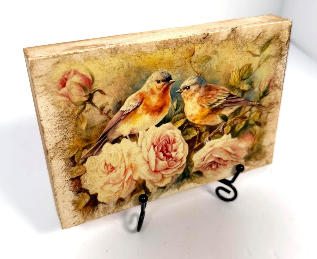 a wooden block with a painting of two birds perched on branches with pink roses.