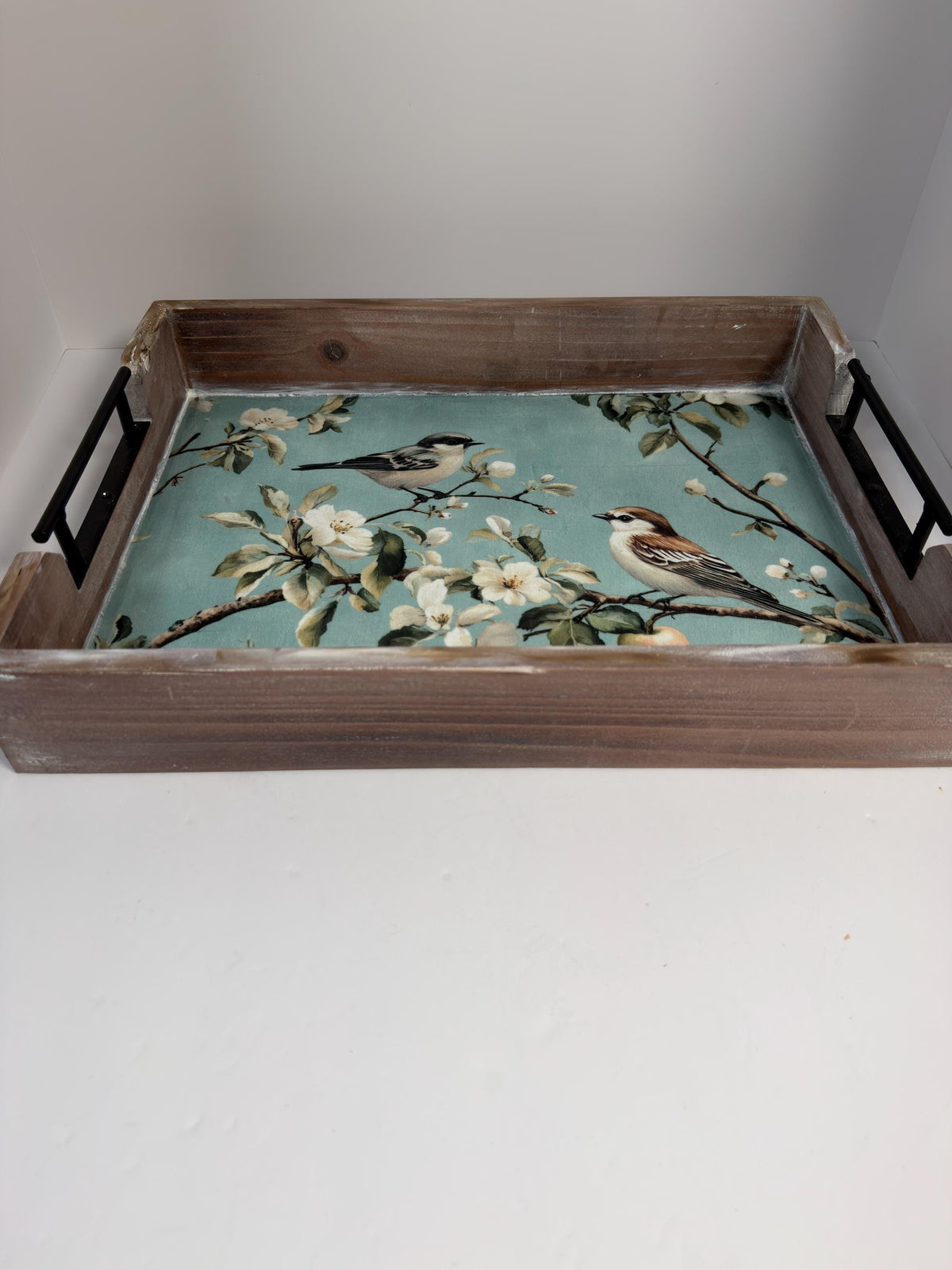 A wooden tray with a floral pattern on it, featuring two birds perched on branches.