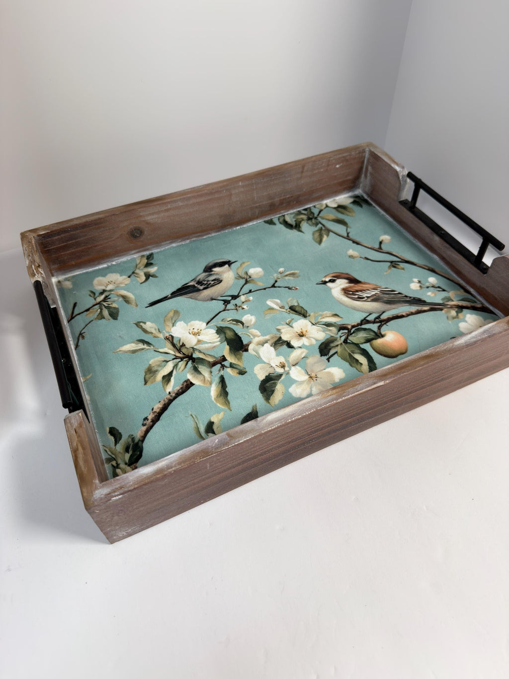 A wooden tray with a floral pattern of white flowers and green leaves, along with two small birds perched on branches.