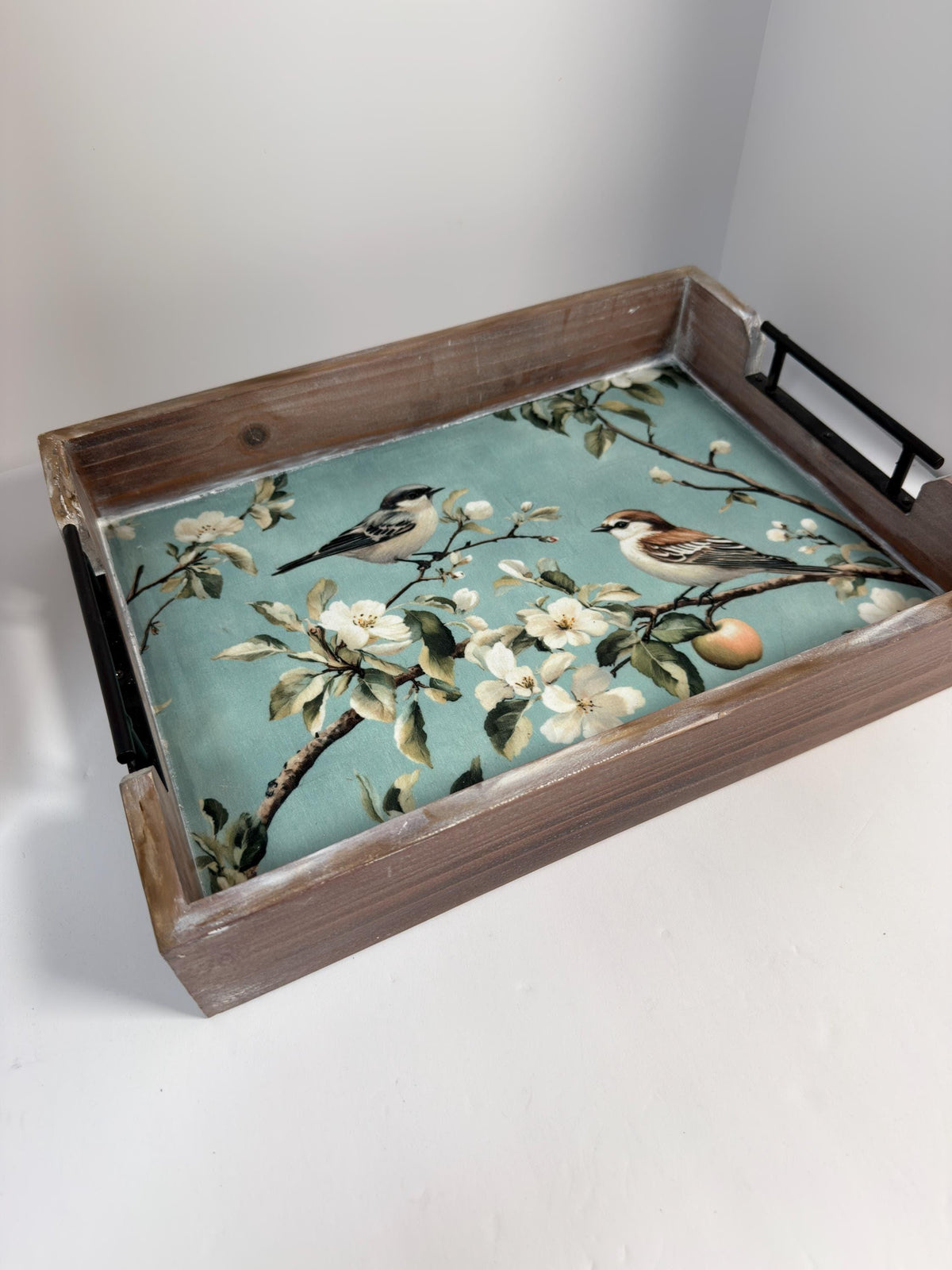A wooden tray with a floral pattern of white flowers and green leaves, along with two small birds perched on branches.