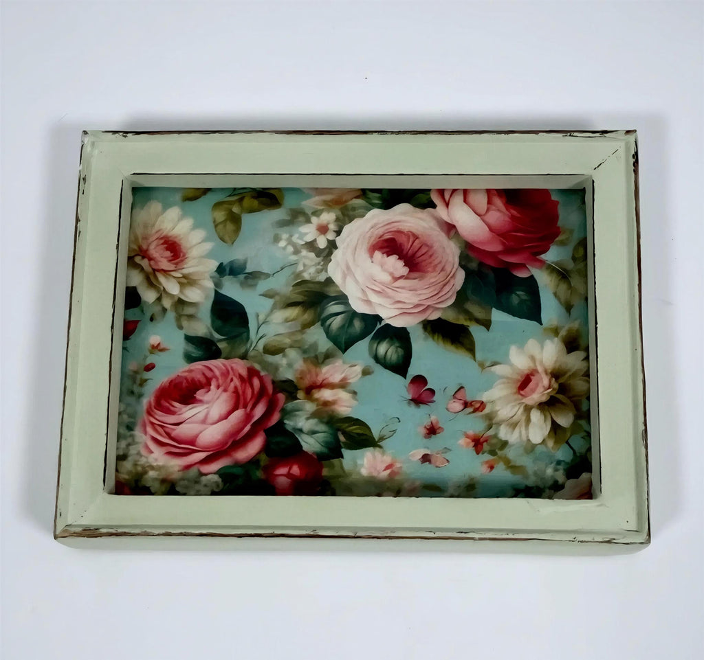 a framed floral print with a vibrant display of pink roses and other flowers against a light blue background.