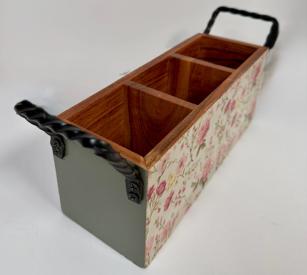 A wooden box with a floral pattern on the front, featuring two handles on either side.