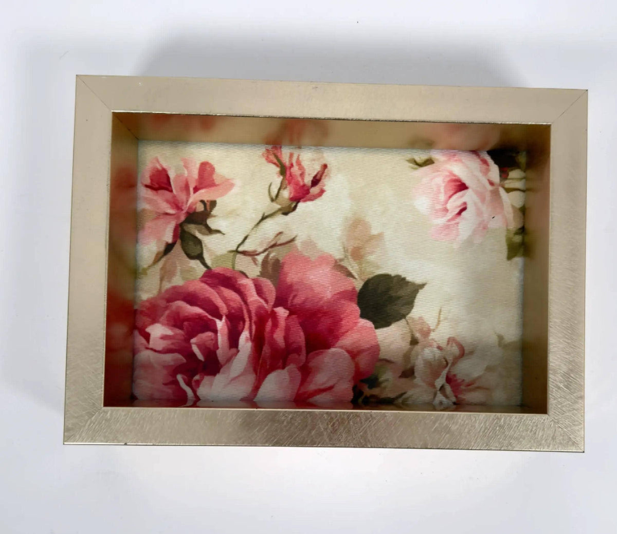 a gold-framed picture of a floral arrangement with pink and red flowers.
