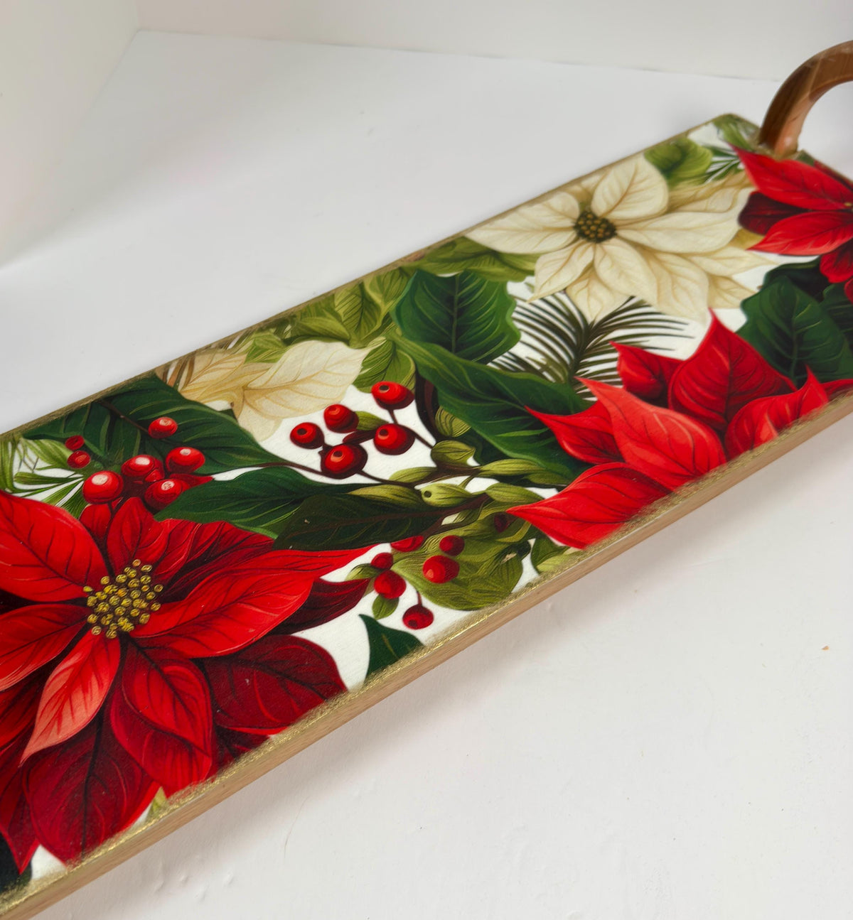 A decorative tray with a floral pattern featuring red poinsettia flowers, green leaves, and red berries.