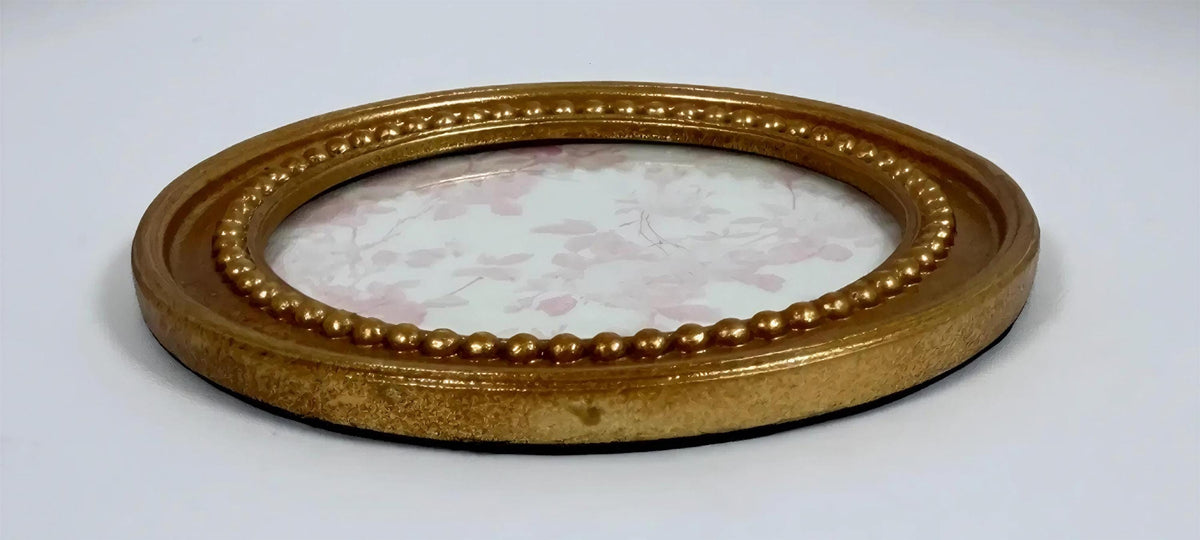 a gold-colored oval frame with a floral pattern on the inside, placed on a white surface.