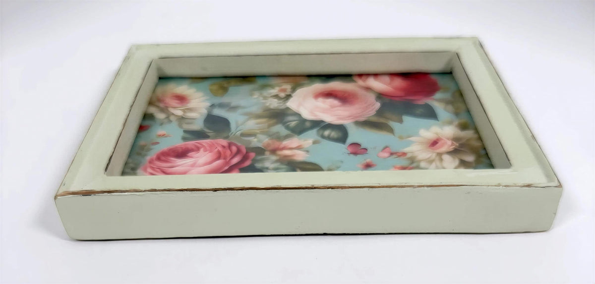 A square, white-framed tray with a floral pattern of pink and white roses on a blue background.