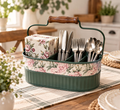A green metal tray with a floral pattern, containing a variety of silverware including forks, knives, and spoons, placed on a wooden table.
