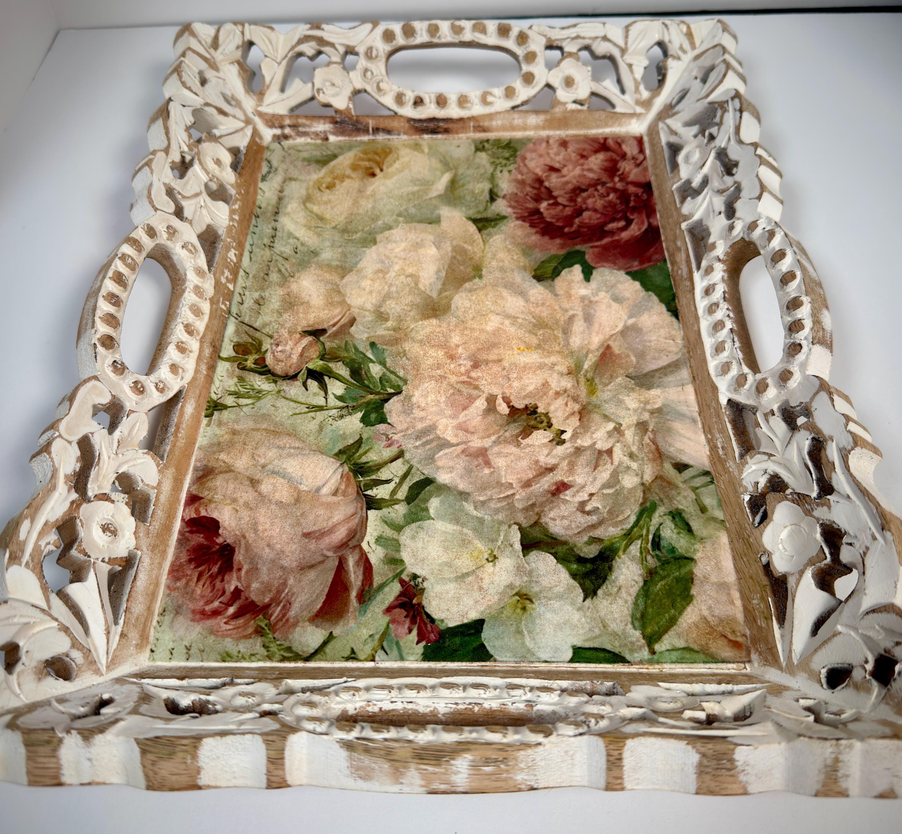 a decorative white tray with an ornate frame, displaying a floral arrangement of white and pink flowers.