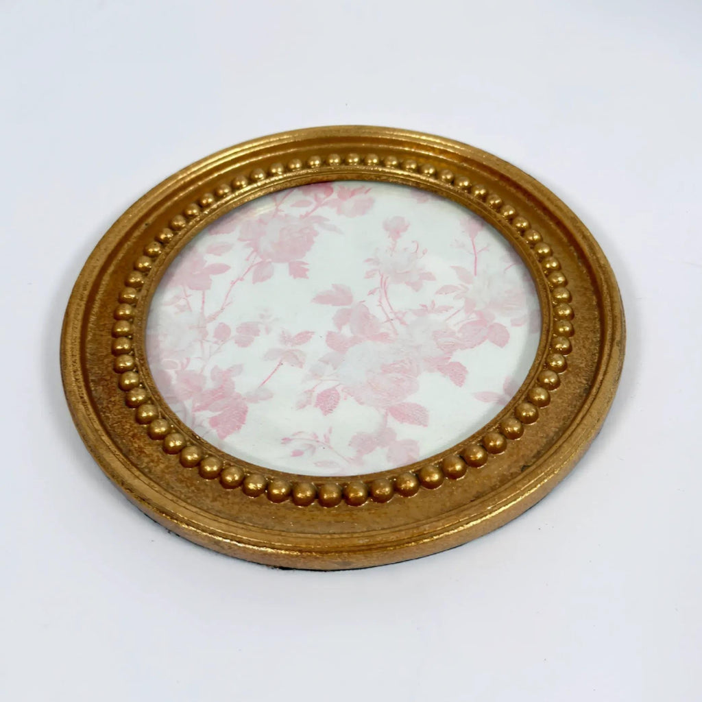 A round gold-colored picture frame with a floral pattern on the inside, placed on a white surface.
