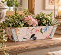 A wooden planter box filled with a variety of colorful flowers and plants, placed on a wooden surface.