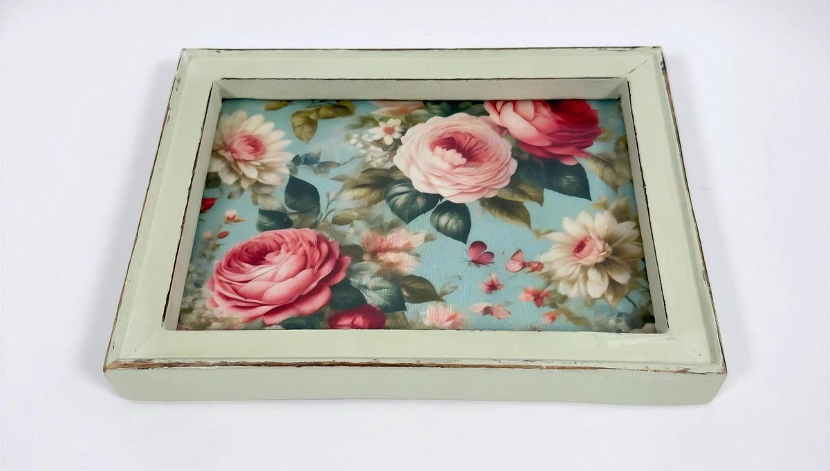 A framed picture of a floral design with pink roses and other flowers against a blue background.