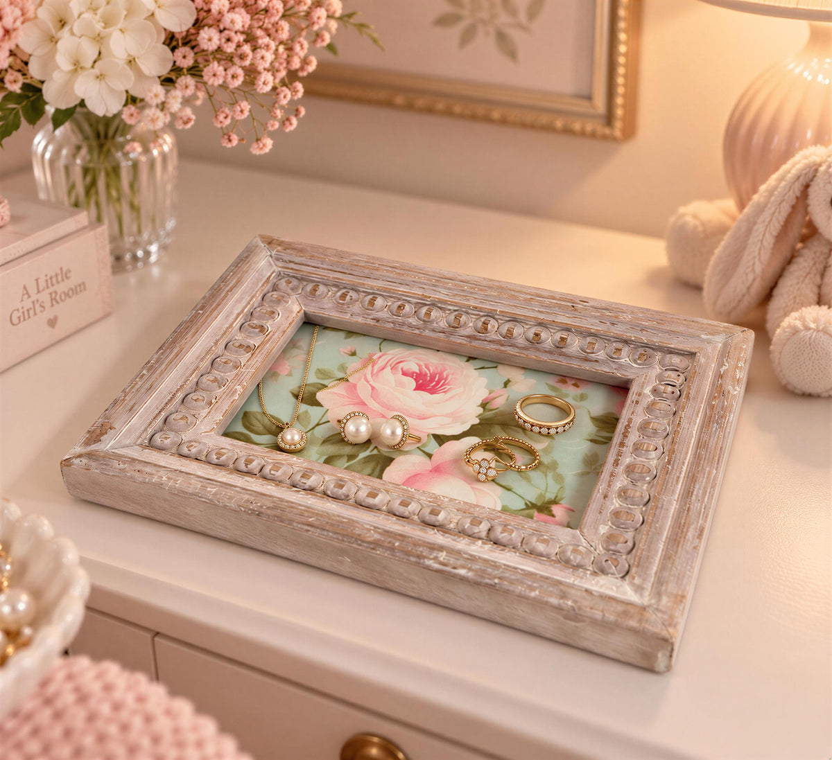 A wooden jewelry box with a floral design sits on a white dresser, displaying various pieces of jewelry such as earrings and rings.