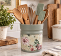 A gray and white floral-patterned canister filled with various kitchen utensils, including wooden spoons, a whisk, and a spatula, sits on a kitchen counter.