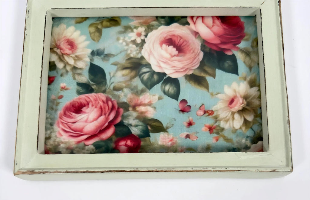 a framed floral print with a vibrant display of pink roses and other flowers against a blue background.