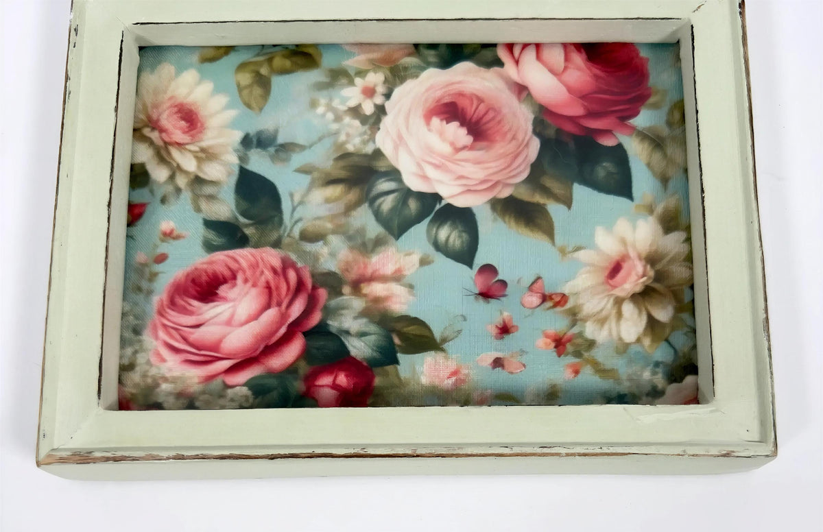 a framed floral print with a vibrant display of pink roses and other flowers against a blue background.