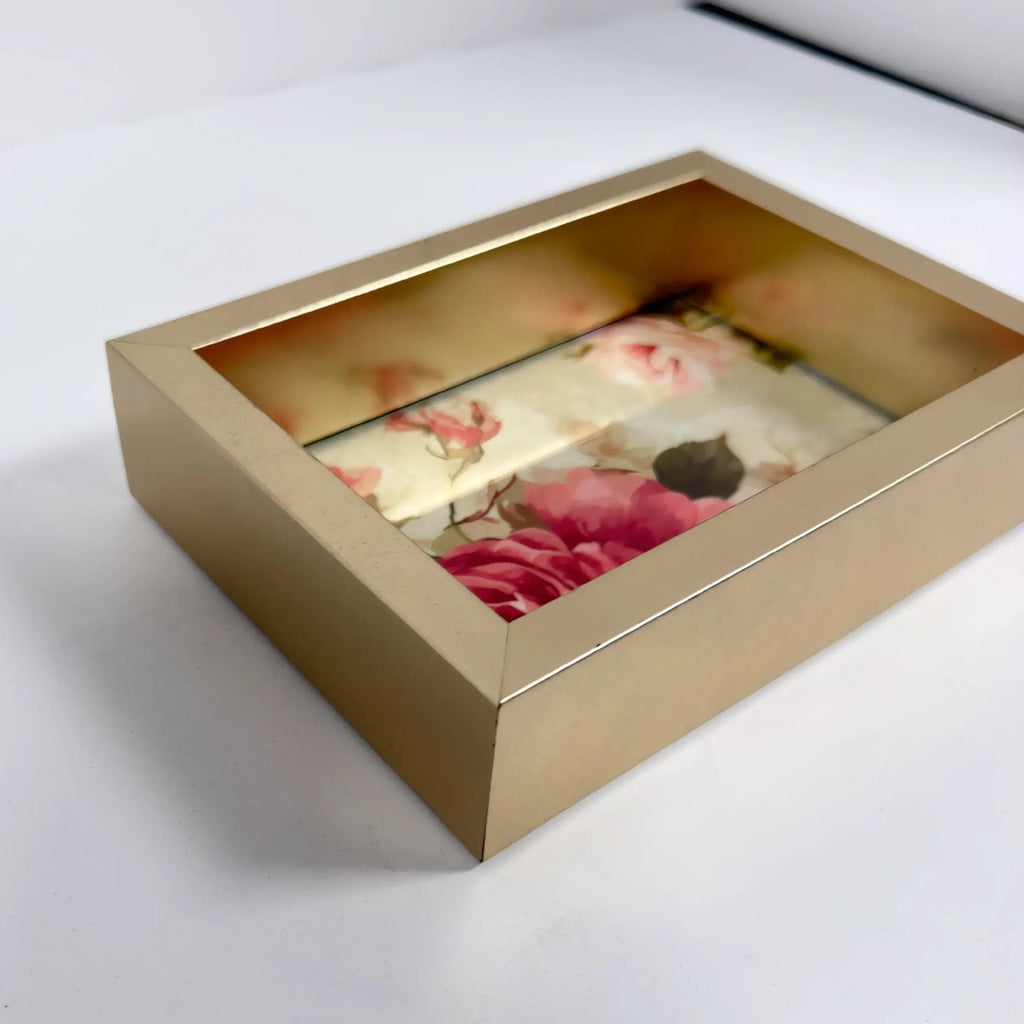 A gold-colored rectangular box with a floral pattern inside, placed on a white surface.