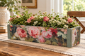 A wooden table with a decorative box featuring a floral design, filled with a variety of colorful flowers and greenery.