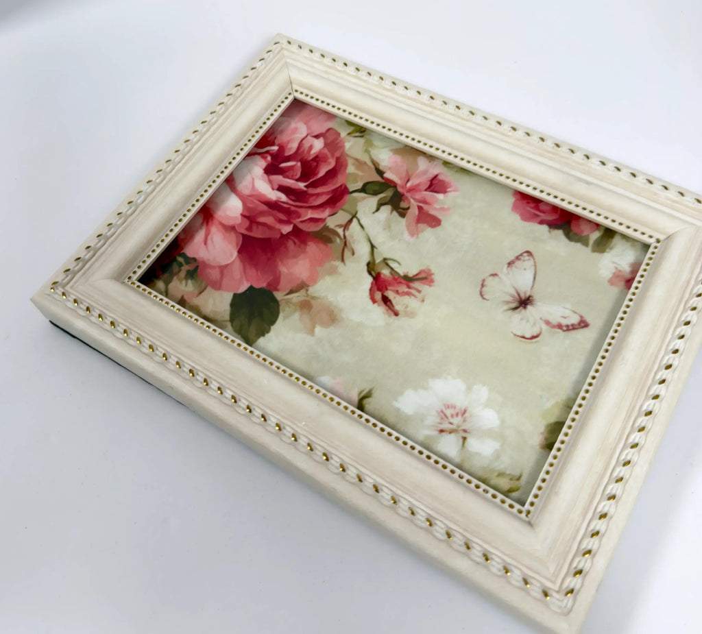 A framed picture with a floral design, featuring a large pink rose and two white flowers, along with a butterfly.