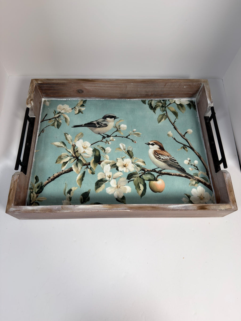 A wooden tray with a floral design featuring two birds perched on branches with flowers and an apple.