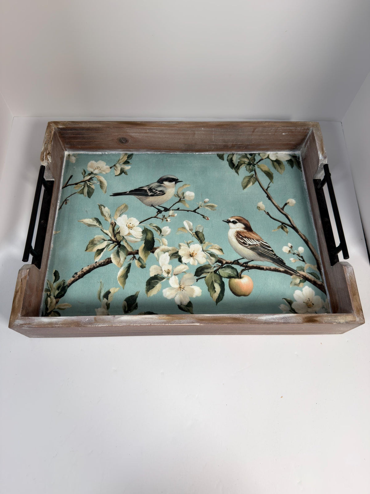 A wooden tray with a floral design featuring two birds perched on branches with flowers and an apple.