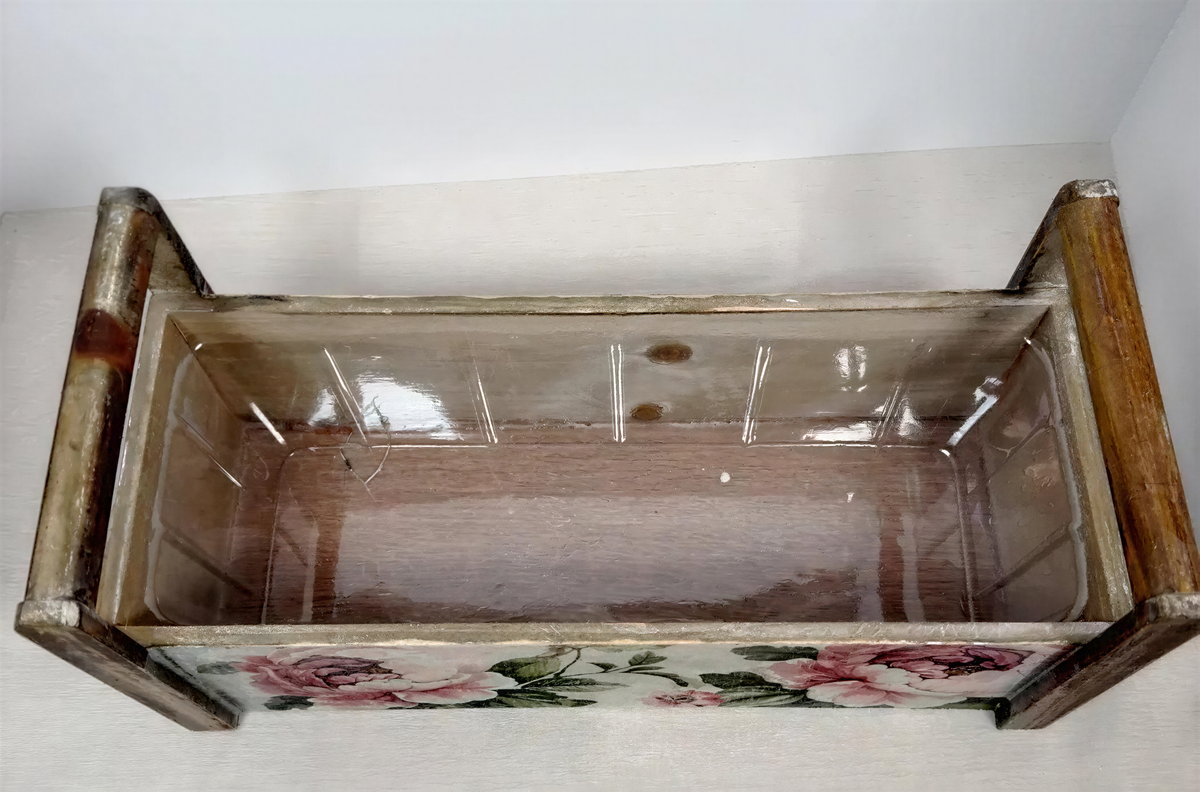 A wooden planter box with a floral design on the front, sitting on a white surface.