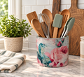 A floral-patterned ceramic container holding various kitchen utensils, including wooden spoons, a whisk, and a spatula, placed on a marble countertop.