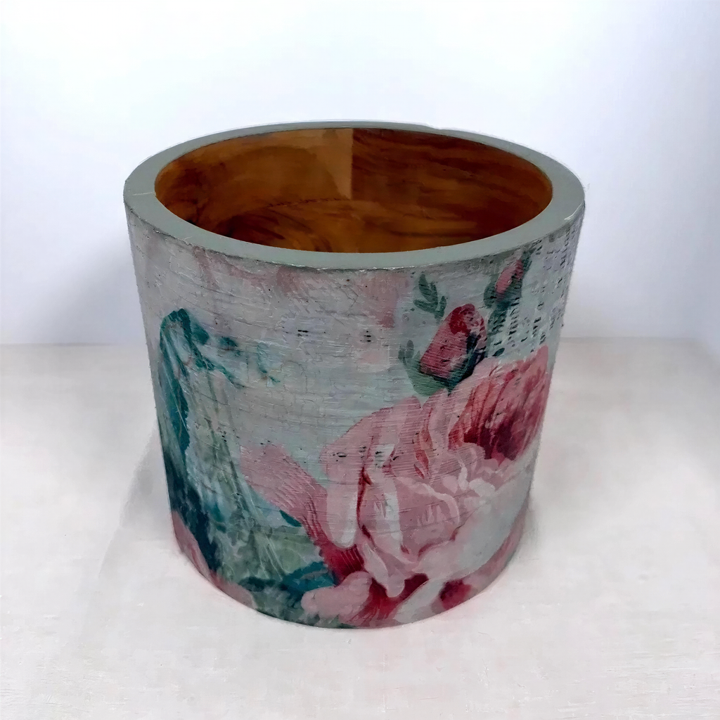A cylindrical container with a floral pattern painted on it, featuring a combination of pink, green, and blue colors.
