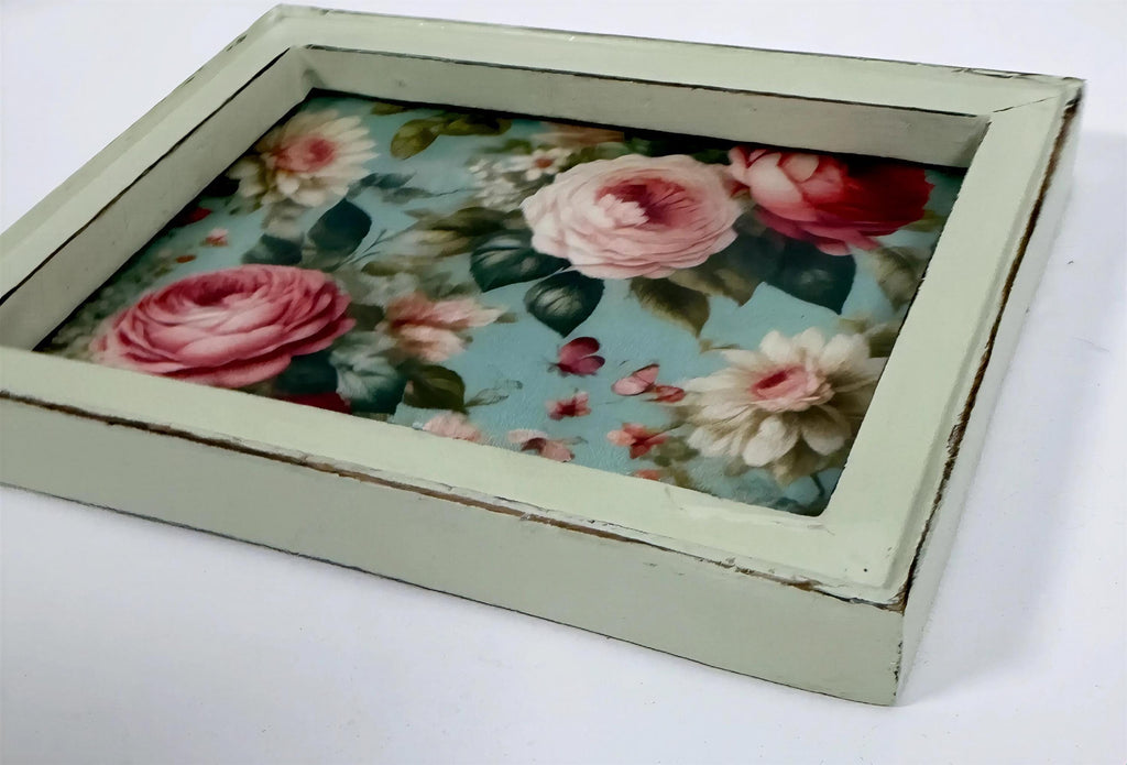 A square wooden frame with a floral pattern of pink and white roses on a blue background.