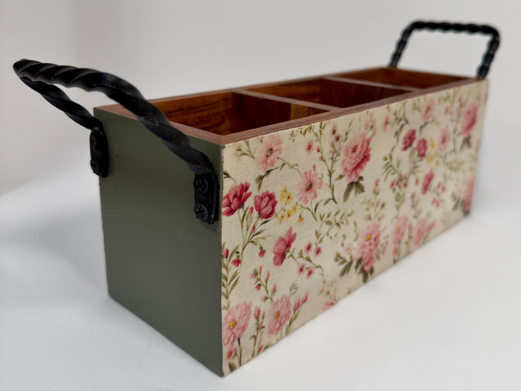 A wooden box with a floral pattern on its side, featuring a black handle on the top.