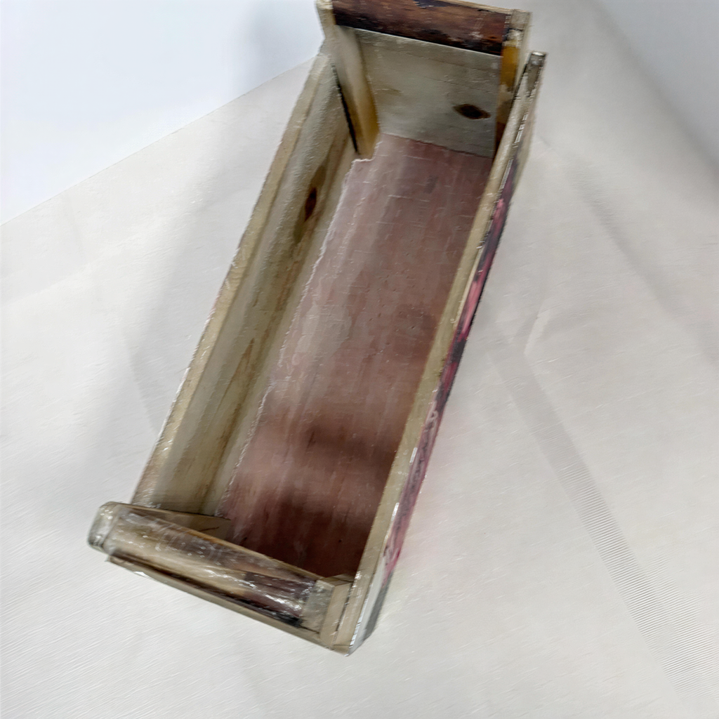 An old, weathered wooden box with a wooden frame and a red interior, sitting on a white surface.