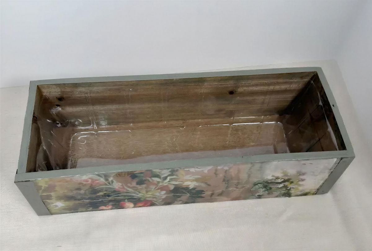 a wooden box with a floral pattern on its side, sitting on a white surface.