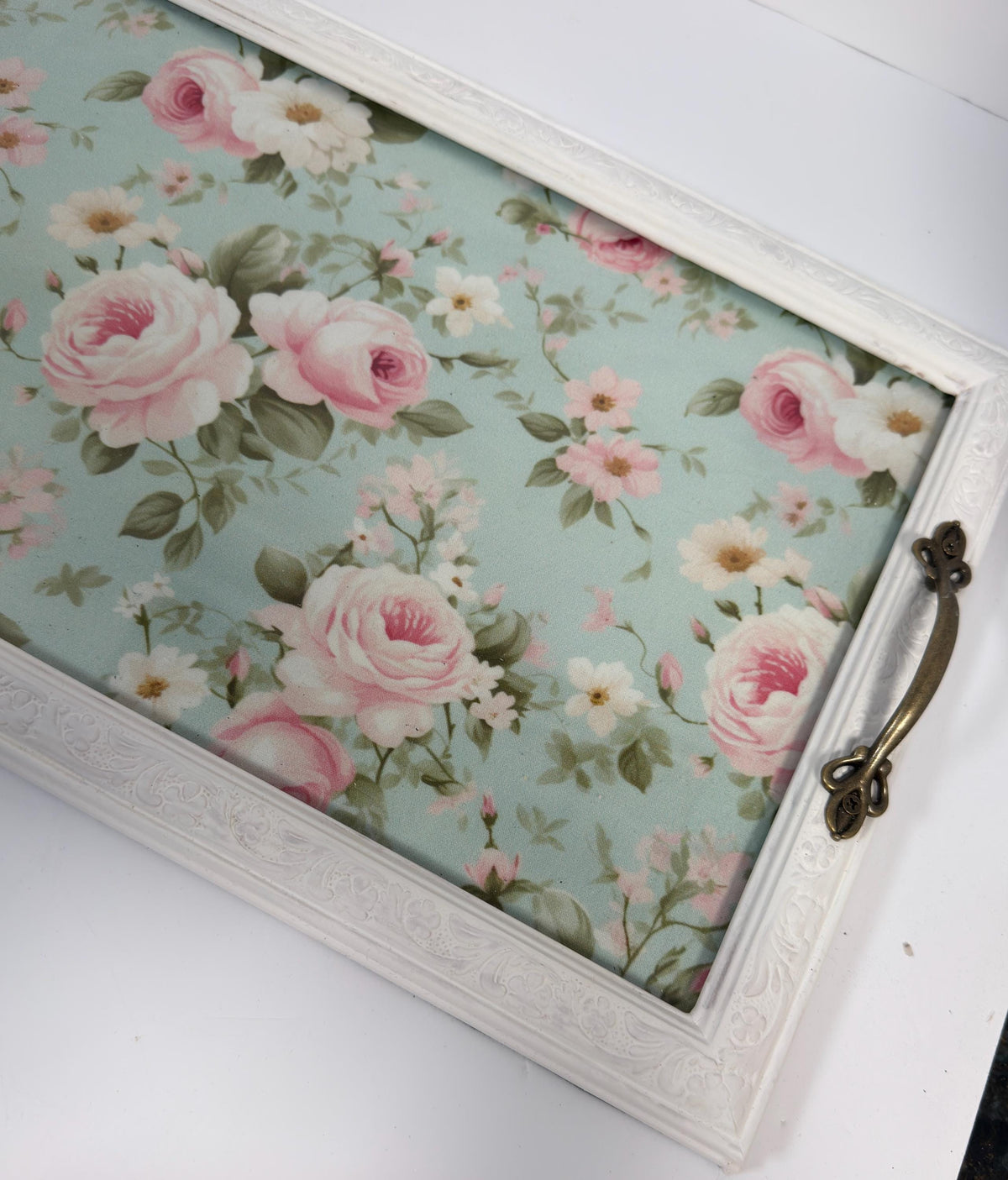A white wooden tray with a floral pattern on it, placed on a white surface.