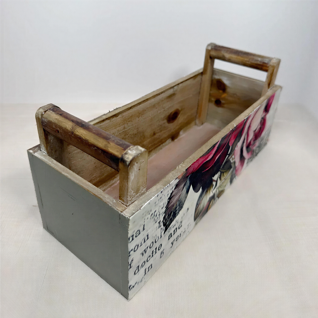 A wooden box with a floral design on the side, sitting on a white surface.