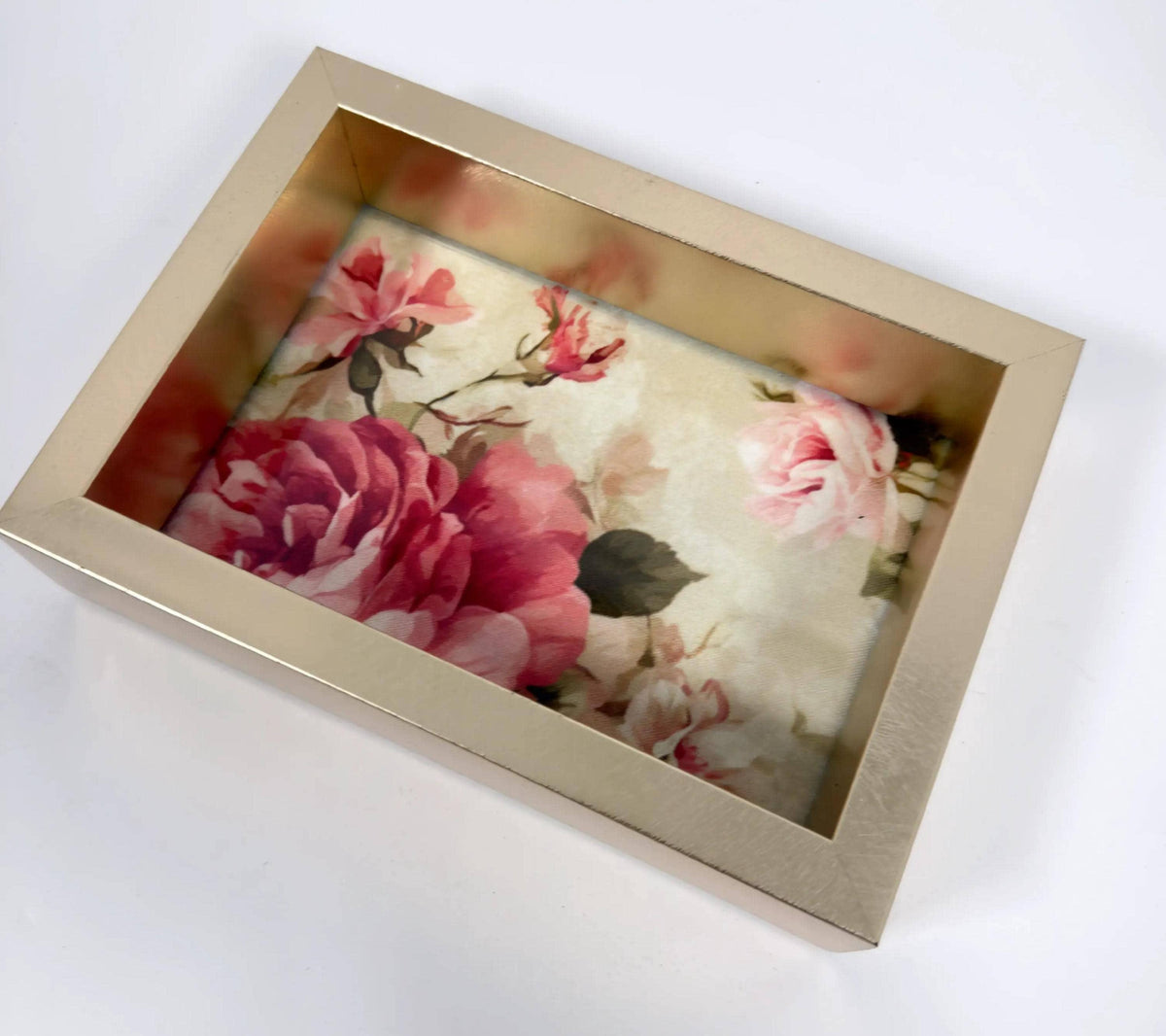 A gold-framed picture frame containing a floral print of pink and white roses.