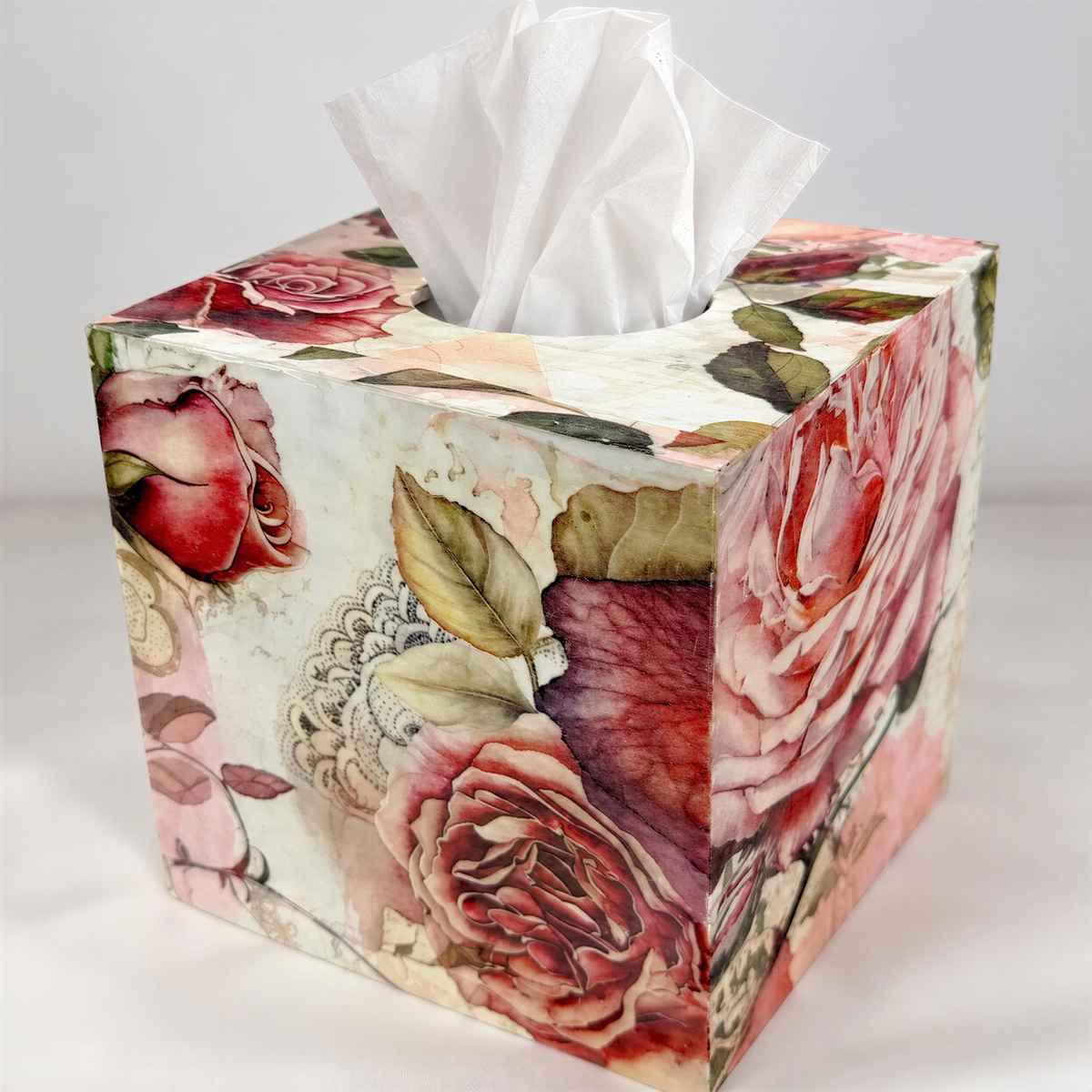A decorative tissue box with a floral pattern, featuring a white tissue paper dispenser and a vibrant design of red and pink roses.