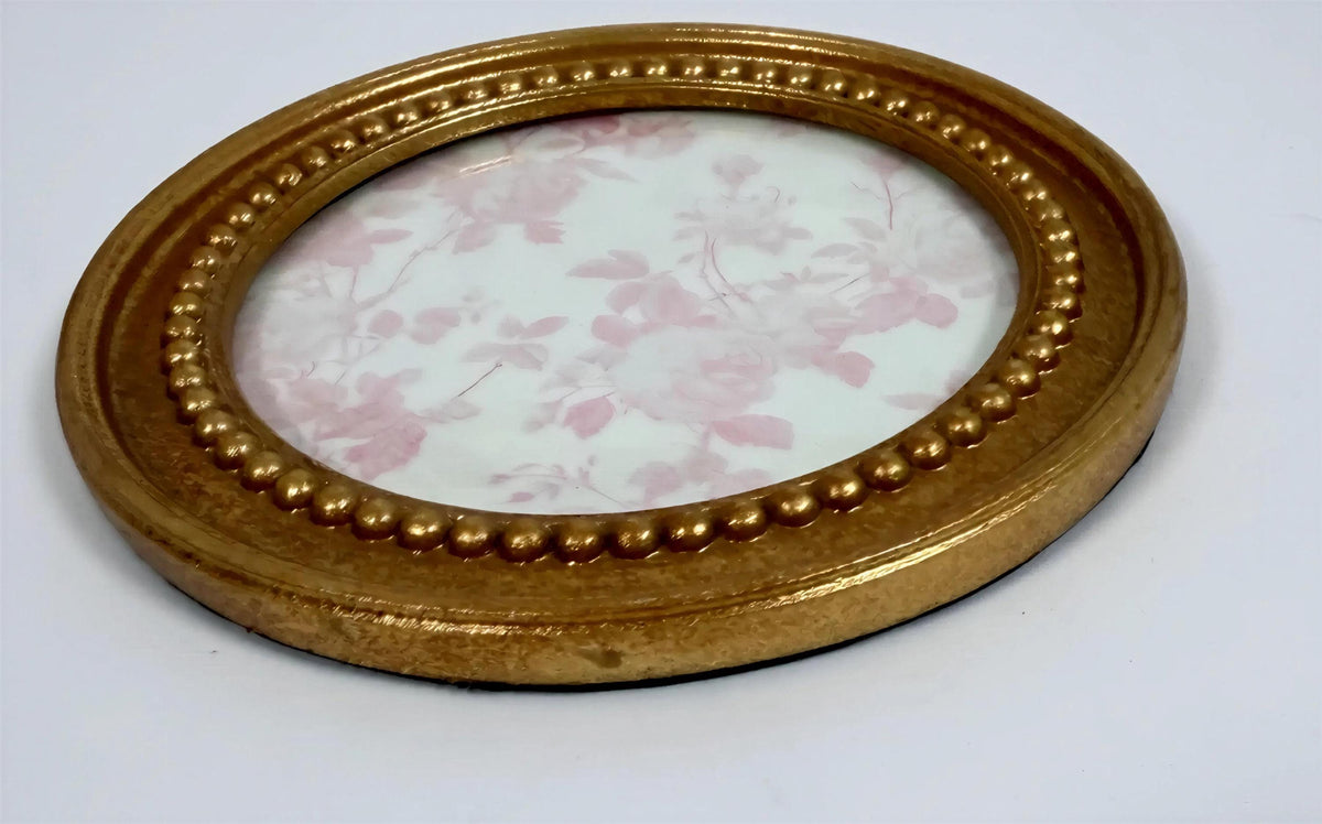 a round gold-colored frame with a floral pattern on the inside, placed on a white surface.