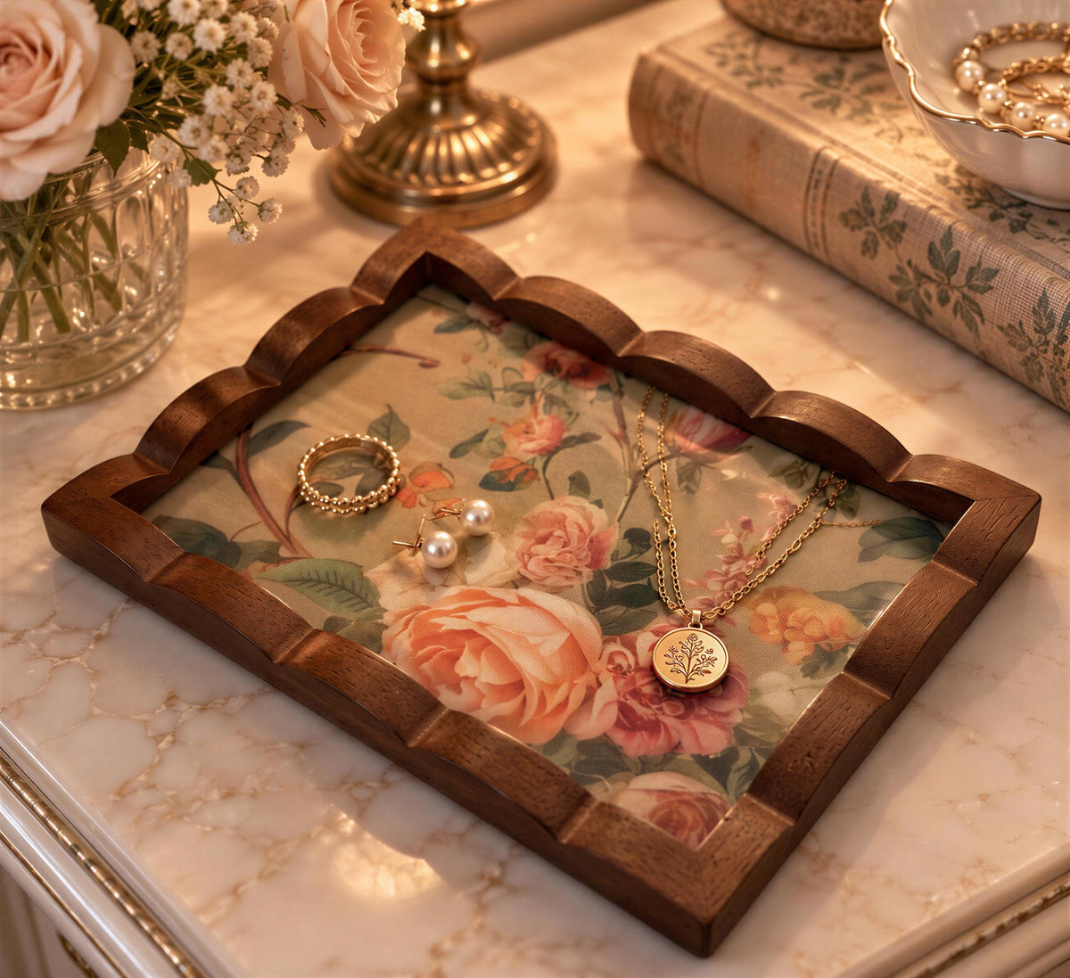 A wooden tray with a floral pattern holds various pieces of jewelry, including a ring, earrings, and a necklace, placed on a marble countertop.