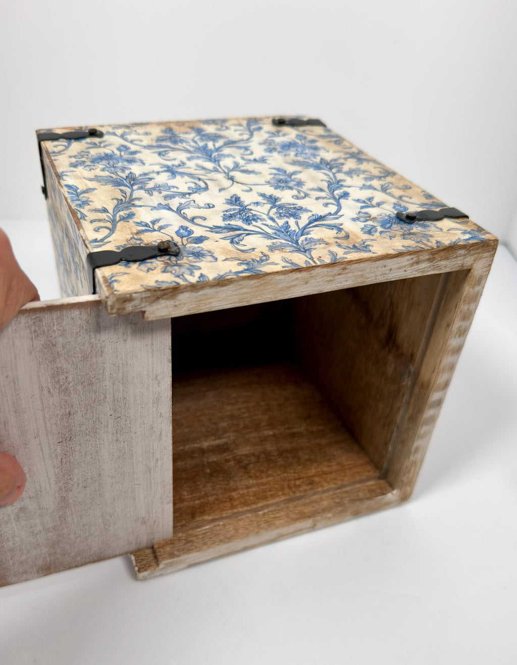 a wooden box with a blue floral pattern on its surface, and a hand is pulling out a piece of the box.