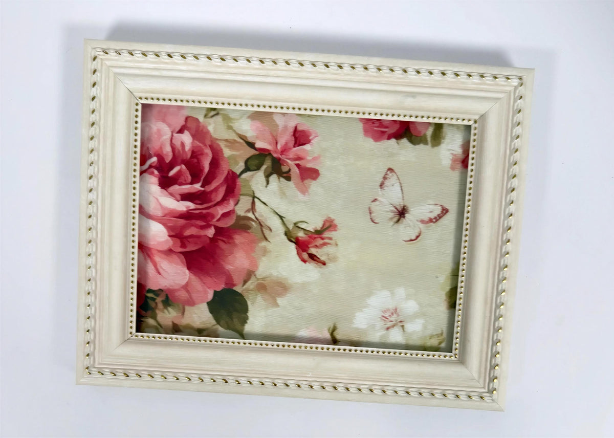 a framed painting of a large pink flower with a butterfly in the background.