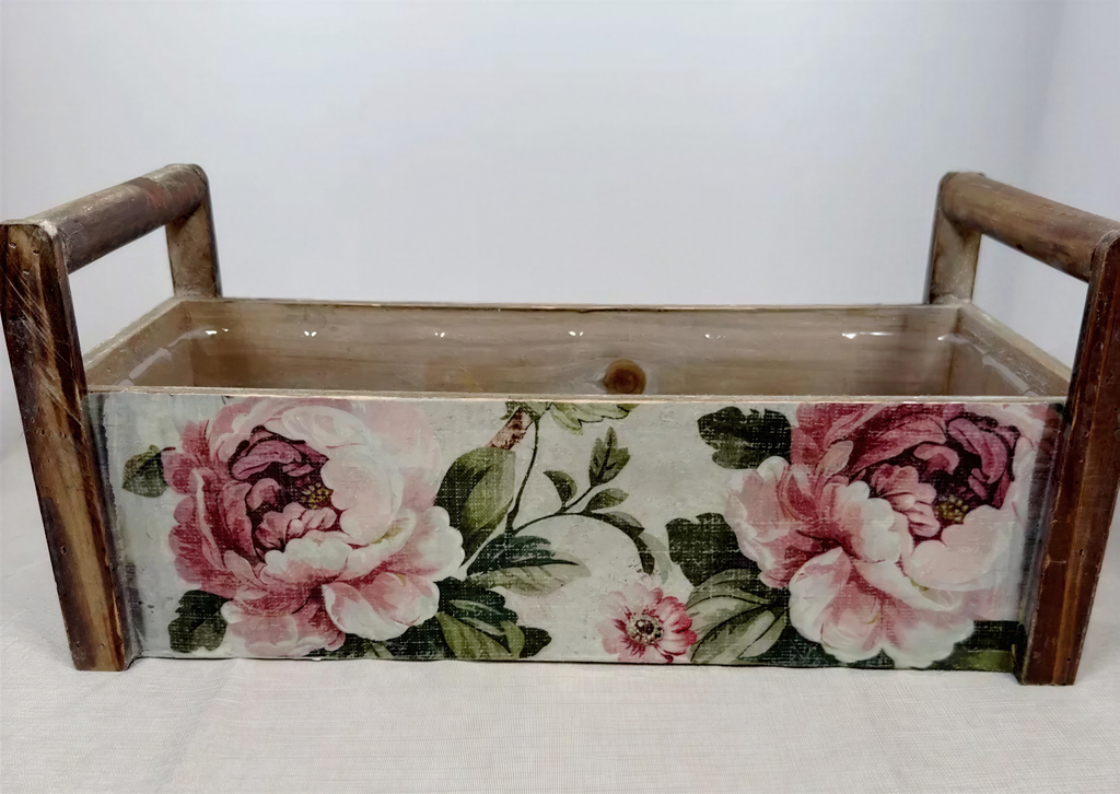 A wooden box with a floral pattern on the front, featuring two large pink flowers and green leaves.